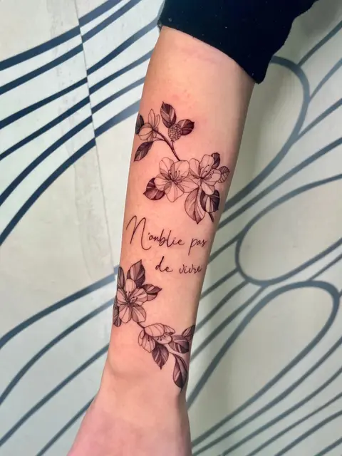 Tatuaggio: fiori di ciliegio in fine line con una scritta in francese sull'avambraccio, di Giada - White Garden Tattoo, Roma Colli Aniene