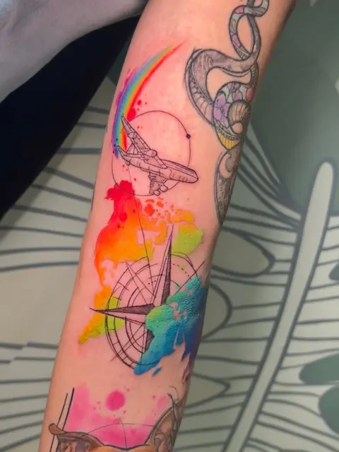 Tatuaggio: composizione di viaggio con aereo, bussola e arcobaleno in watercolor, di Giada - White Garden Tattoo, Roma Colli Aniene