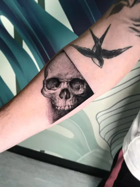 Tatuaggio: teschio realistico con rondine sull'avambraccio, di Massimiliano - White Garden Tattoo, Roma Colli Aniene